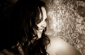 A black and white photo of Aidy looking sideways, face half covered by her tumble of hair with a disco bright background